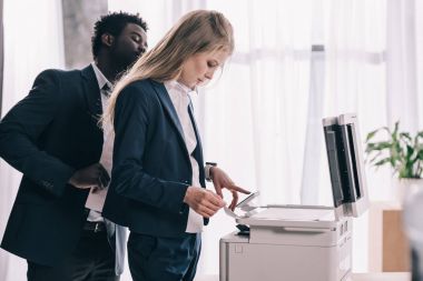 young businesspeople using copier together at office clipart