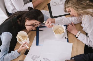 top view of businesswomen sleeping on table with boxes of noodles with chopsticks at office clipart