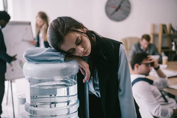 exhausted zombie like manager leaning on water dispenser at office