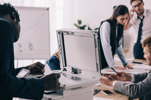 african american manager using copier in conference hall with colleagues blurred on background