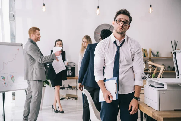 Bewildered Overworked Businessman Standing Office Blurred Colleagues Working Background — Stock Photo, Image