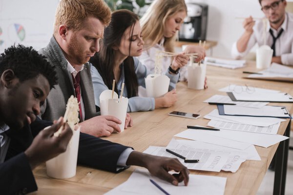 exhausted businesspeople eating noodles while having paperwork at office