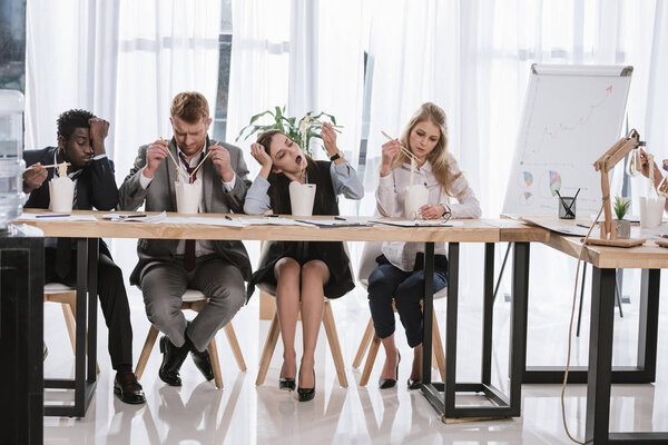 group of tired managers eating noodles together at office