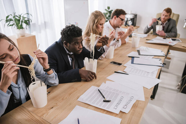businesspeople eating noodles together at office while having conversation