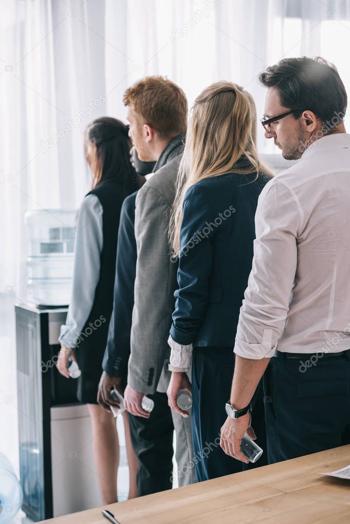 overworked managers standing in queue for water dispenser at office