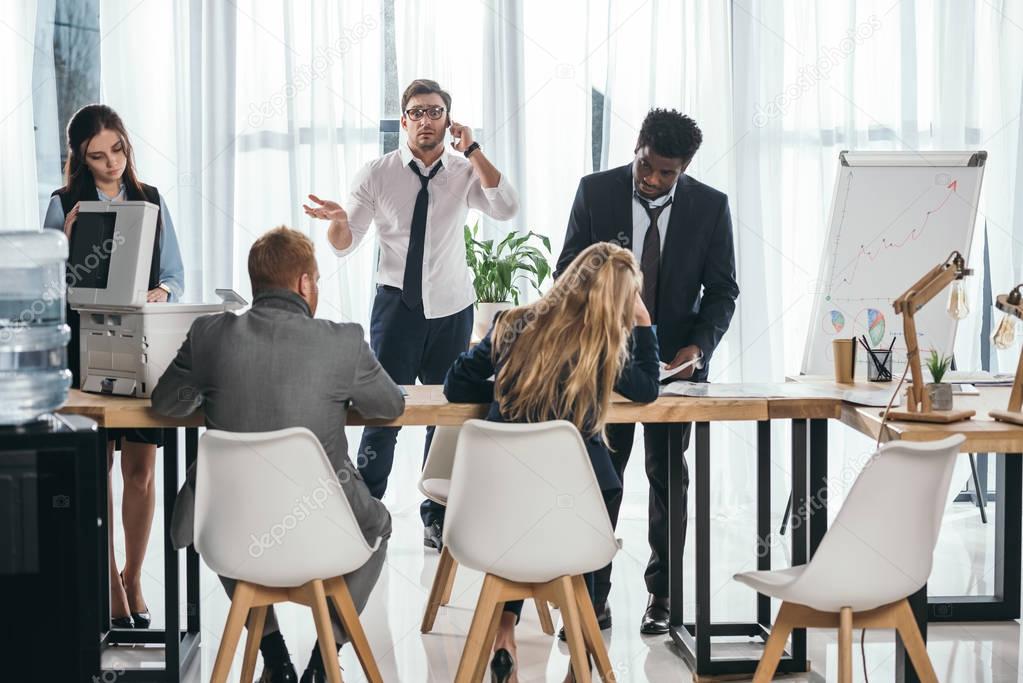 group of businesspeople having conversation at office while boss talking by phone