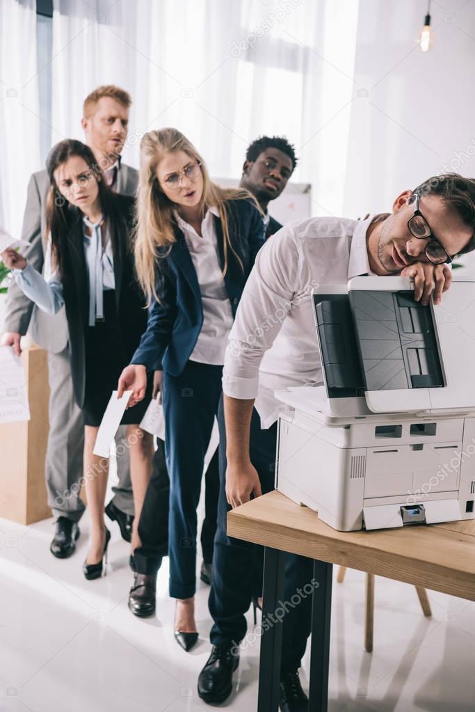 businessman sleeping on copier while his colleagues standing in queue behind him