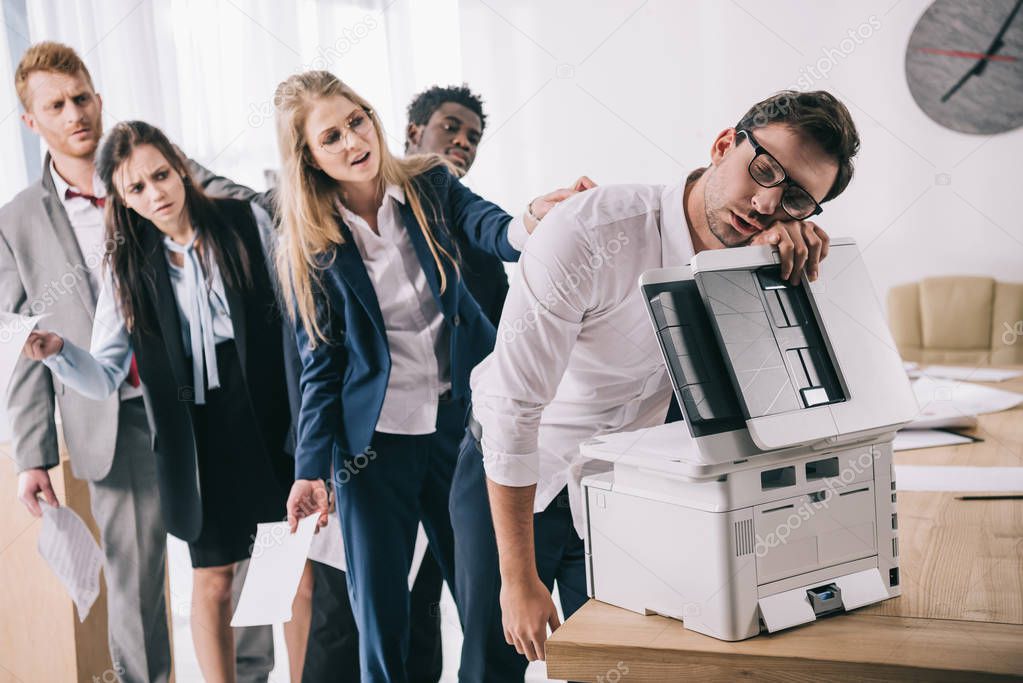 exhausted businessman sleeping on copier while his colleagues standing in queue behind him