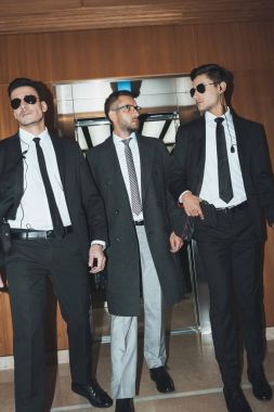 bodyguards and businessman walking from elevator in business center clipart