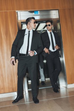 bodyguards reviewing territory when going out from elevator with businessman  clipart