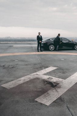 bodyguard and businessman standing near car on helipad clipart