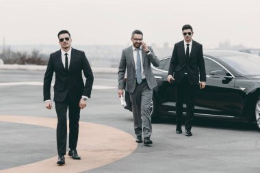 araç ve smartphone ile konuşurken korumayla yürüyüş işadamı gülümseyen  