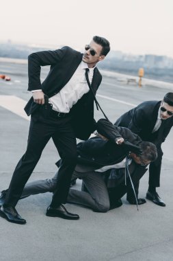 two bodyguards in sunglasses protecting falling businessman   clipart