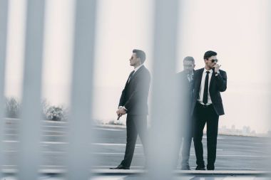 view through fence of businessman with bodyguards standing on helipad clipart