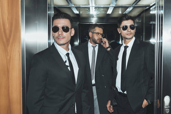bodyguards reviewing territory when businessman talking by smartphone in elevator