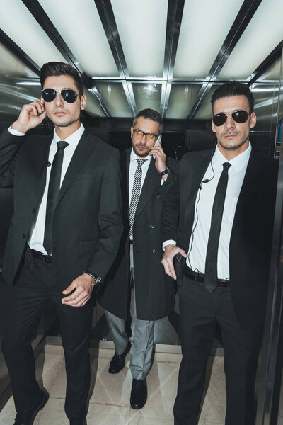 бизнесмен разговаривает по смартфону и идет с телохранителями
