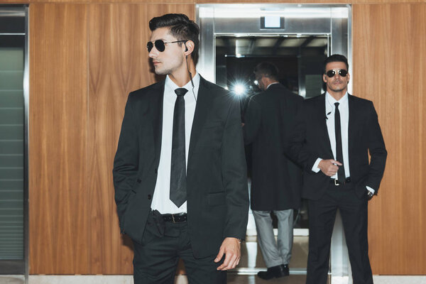 two bodyguards in sunglasses waiting for businessman at elevator