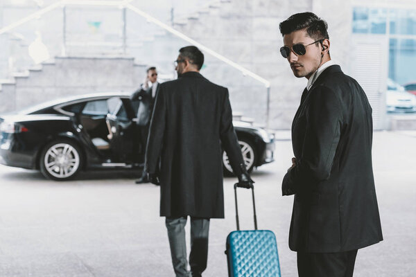 businessman going with blue wheeled bag to car 