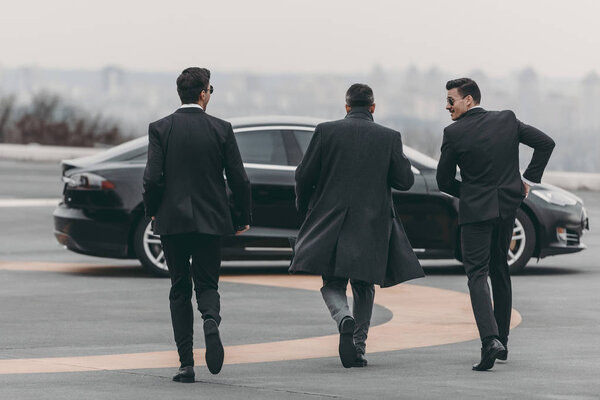rear view of businessman and bodyguards walking to car at helipad