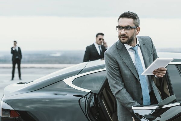 businessman going out from car and holding tablet in hand