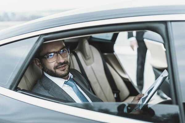 businessman sitting in a car with newspaper and looking away