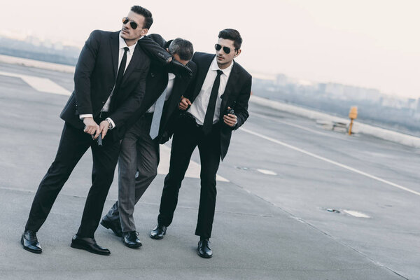 two bodyguards in sunglasses protecting businessman with gun 