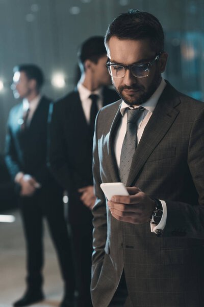 красивый бизнесмен стоит и смотрит на смартфон
 