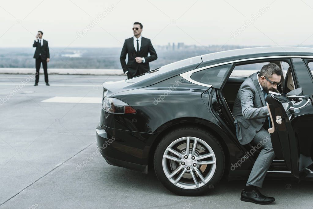 businessman in gray suit going out from black car