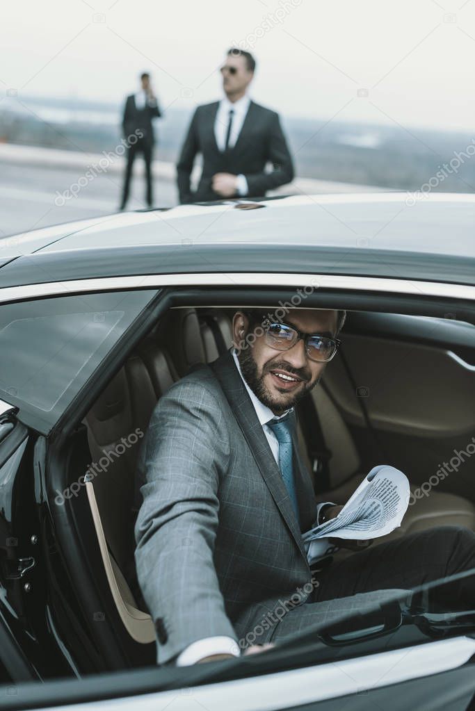smiling businessman in glasses going out from car