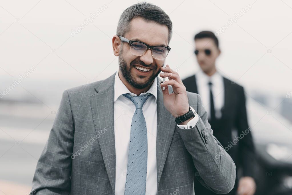 smiling businessman with bodyguard talking by smartphone