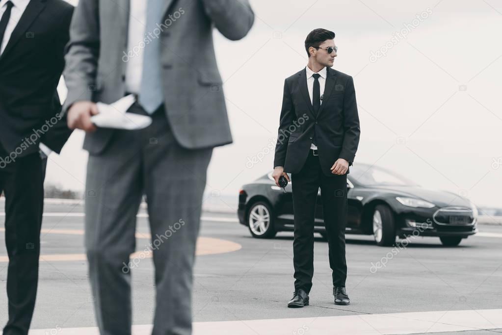 cropped image of bodyguards and businessman walking on helipad from car