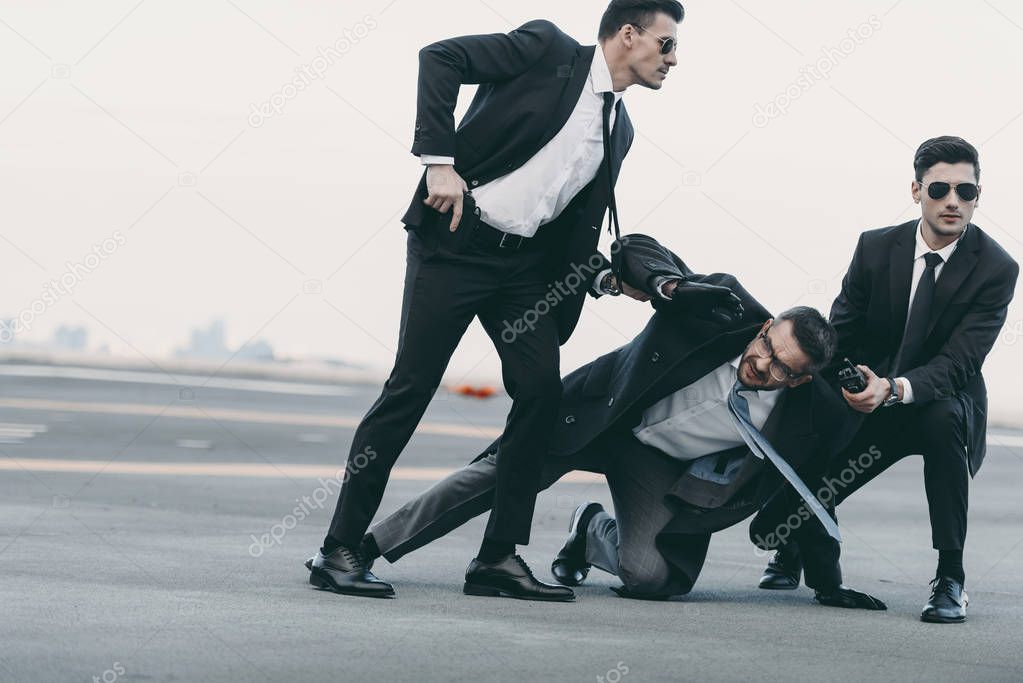 two bodyguards in sunglasses protecting falling businessman 