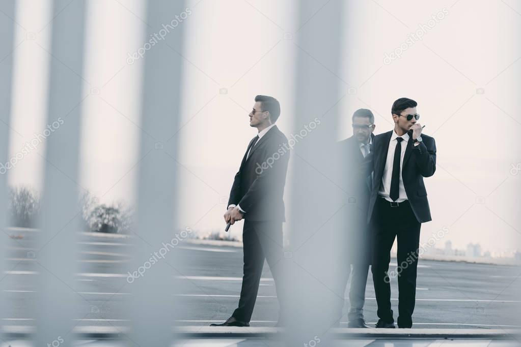 view through fence of businessman with bodyguards standing on helipad