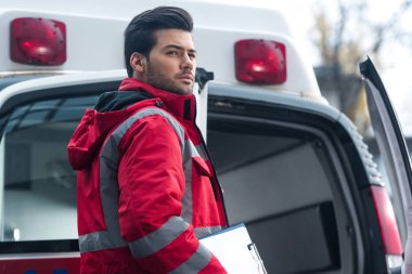 ayakta ve uzağa bakarak ciddi yakışıklı erkek sağlık görevlisi