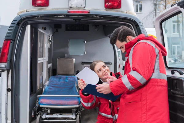 Felizes Paramédicos Masculinos Femininos Lendo Documentos Frente Ambulância — Fotografia de Stock