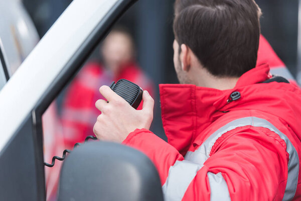 male paramedic talking by portable radio and showing something to colleague