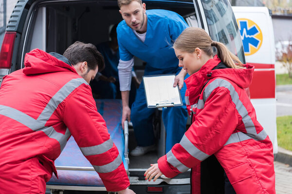 young paramedics moving ambulance stretcher from car