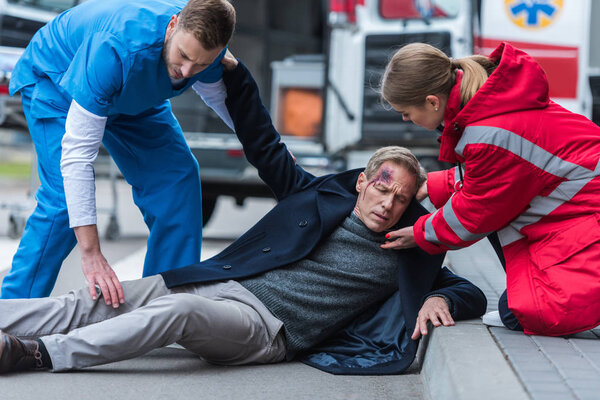 молодые мужчины и женщины-парамедики помогают раненому человеку на улице
