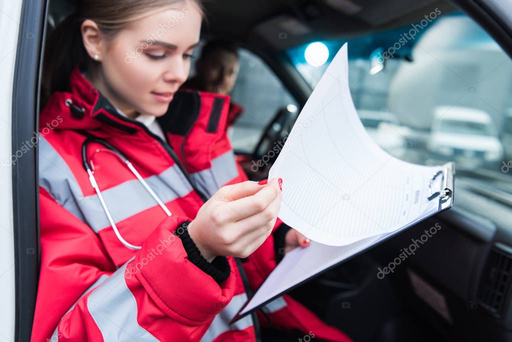 female paramedic sitting in ambulance and looking at clipboard