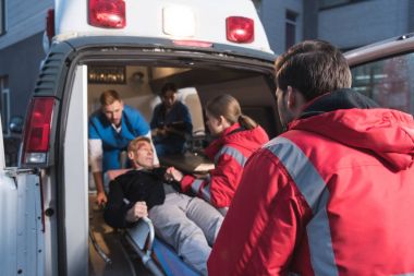 team of paramedics moving wounded mature man into ambulance clipart