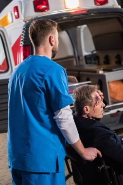 Olgun adam ambulans için tekerlekli sandalye üzerinde hareket sağlık görevlisi yaralı