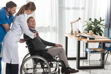 kadın doktor olgun adam için tekerlekli sandalye üzerinde konuşuyor