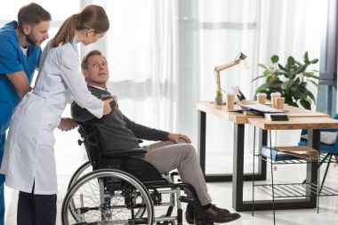 female doctor talking to mature man on wheelchair clipart