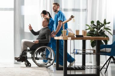 Nurses helping middle aged man on wheelchair clipart