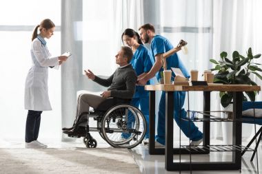 female doctor talking with middle aged patient on wheelchair  clipart