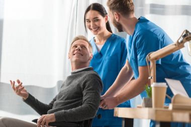 smiling doctors and patient on wheelchair talking in the hospital clipart