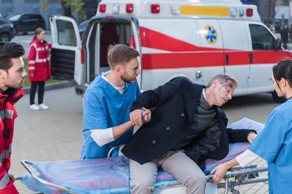 Jóvenes Paramédicos Ayudando Hombre Herido Acostado Camilla Ambulancia — Foto de Stock