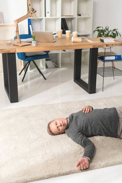 мужчина средних лет без сознания лежит на полу в офисе
