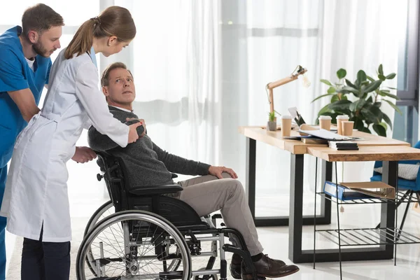kadın doktor olgun adam için tekerlekli sandalye üzerinde konuşuyor