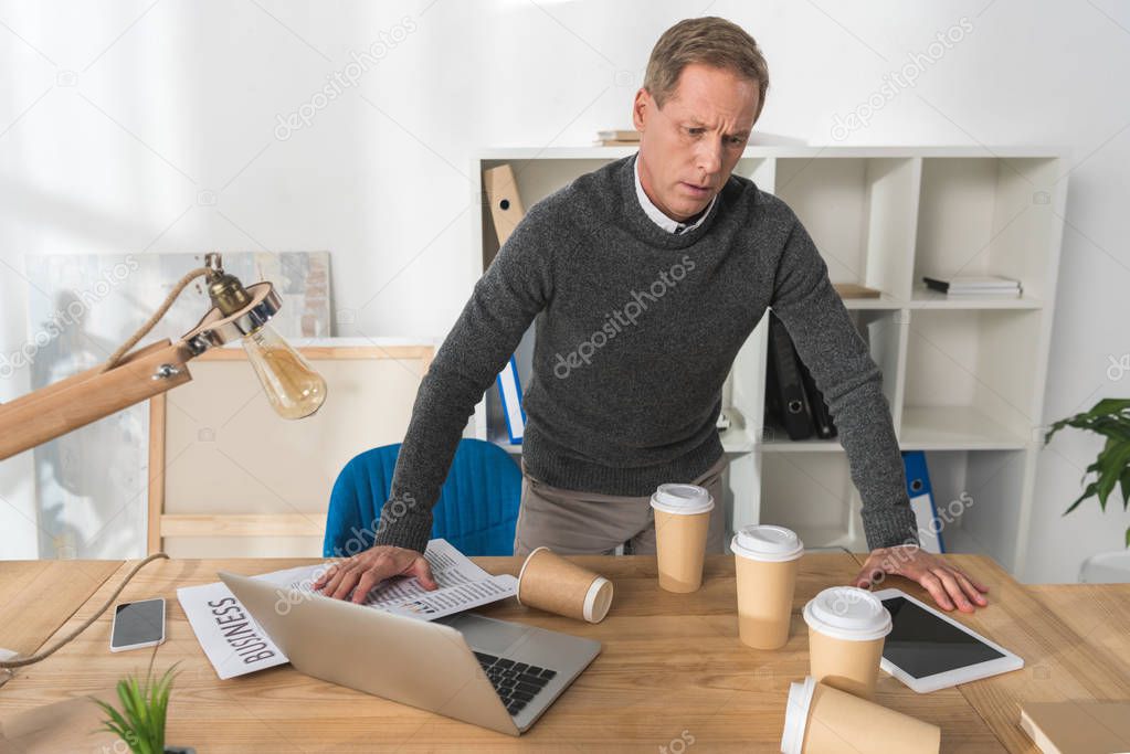 mature man feeling bad and leaning on table in office